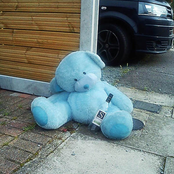 Abandoned, Unwanted, Unloved, cuddly toy - Large pale blue teddybear with an empty wine bottle, slumped against a driveway fence 
