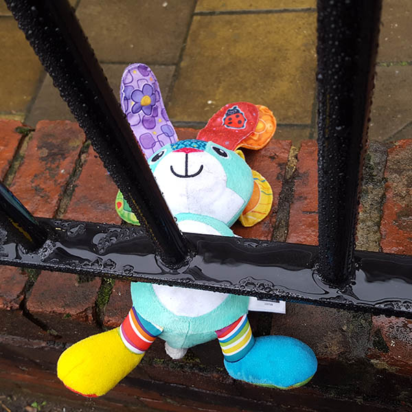 Abandoned cuddly toy colourful bunny underneath railings