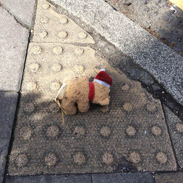 Abandoned, unwanted, unloved, cuddly toy - Teddybear, wearing a santa hat and scarf, face down, on the pavement