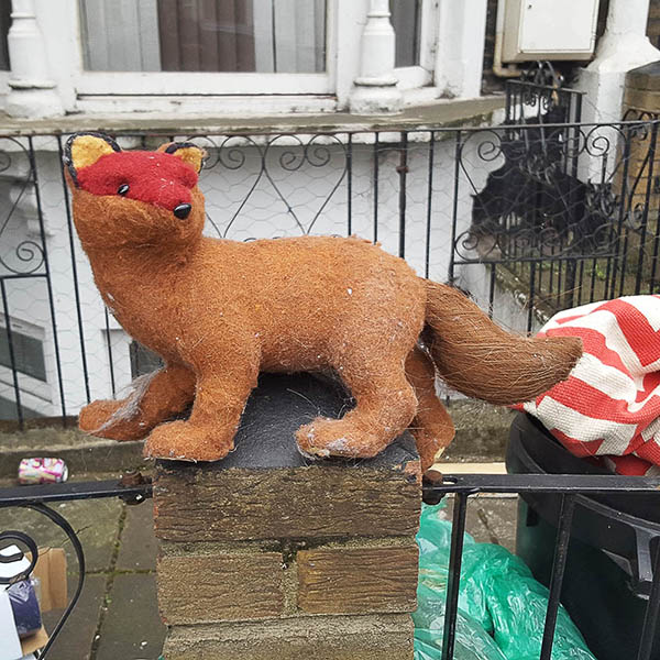 Abandoned, unwanted, unloved, cuddly toy - cuddly fox standing on a wall in front of a house