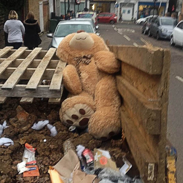 Abandoned, unwanted, unloved, cuddly toy - Huge, pale brown teddybear with a tartan bowtie, lying in a skip amongst the rubble and rubbish