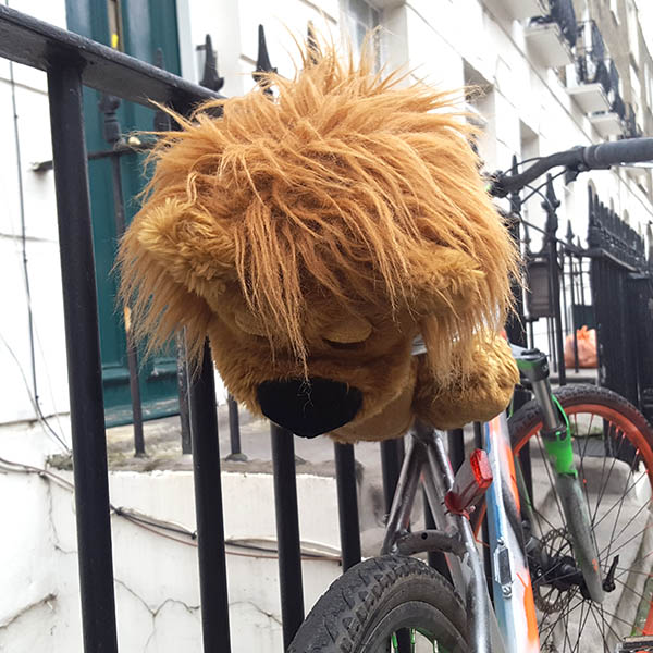 Cuddly toy lion on a bike chained to a railing