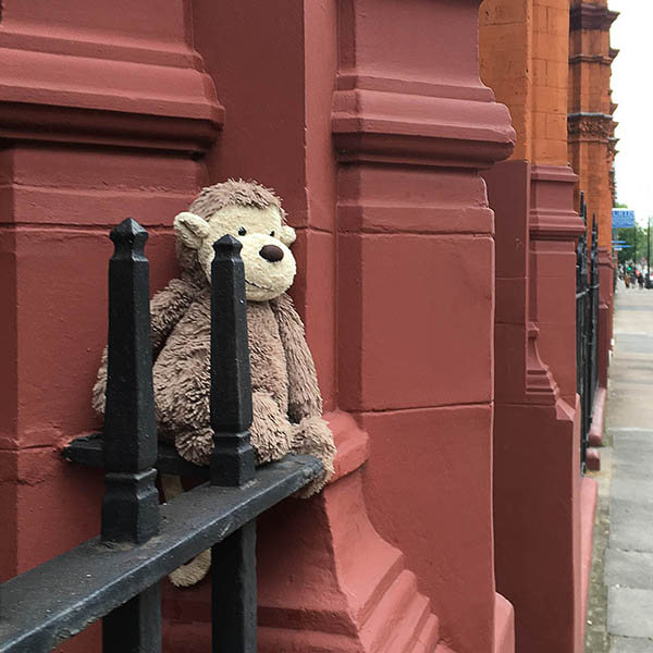 Abandoned, unwanted, unloved, cuddly toy - Cuddly monkey sat on a railing, leaning against a building, looking pensive 