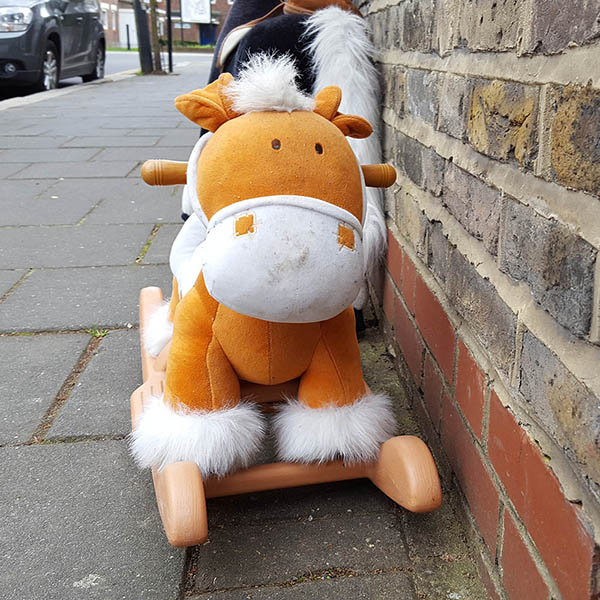 Abandoned, unwanted, unloved, cuddly toy - Cuddly, orange rocking horse, left on the Pavement next to a brick wall
