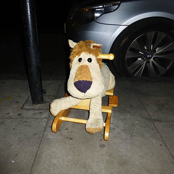 Abandoned, unwanted, unloved, cuddly toy - Cuddly rocking lion on the pavement curbside, next to a lamp post