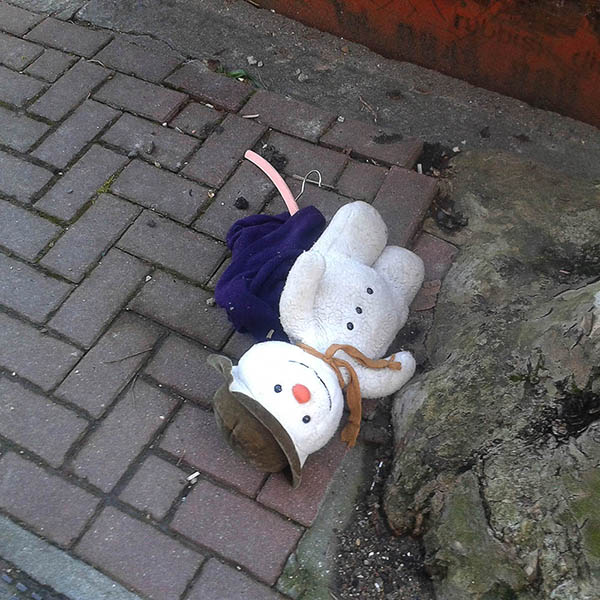 Abandoned, unwanted, unloved, cuddly toy - Cuddly snowman with a big smile, wearing a hat and scarf, lying by a tree