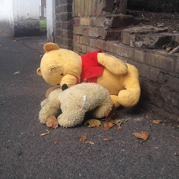 Abandoned, unwanted, unloved, cuddly toy - Cuddly Winnie the Pooh teddybear, slumped over a fluffy, beige teddybear, face down on the pavement next to a broken brick wall