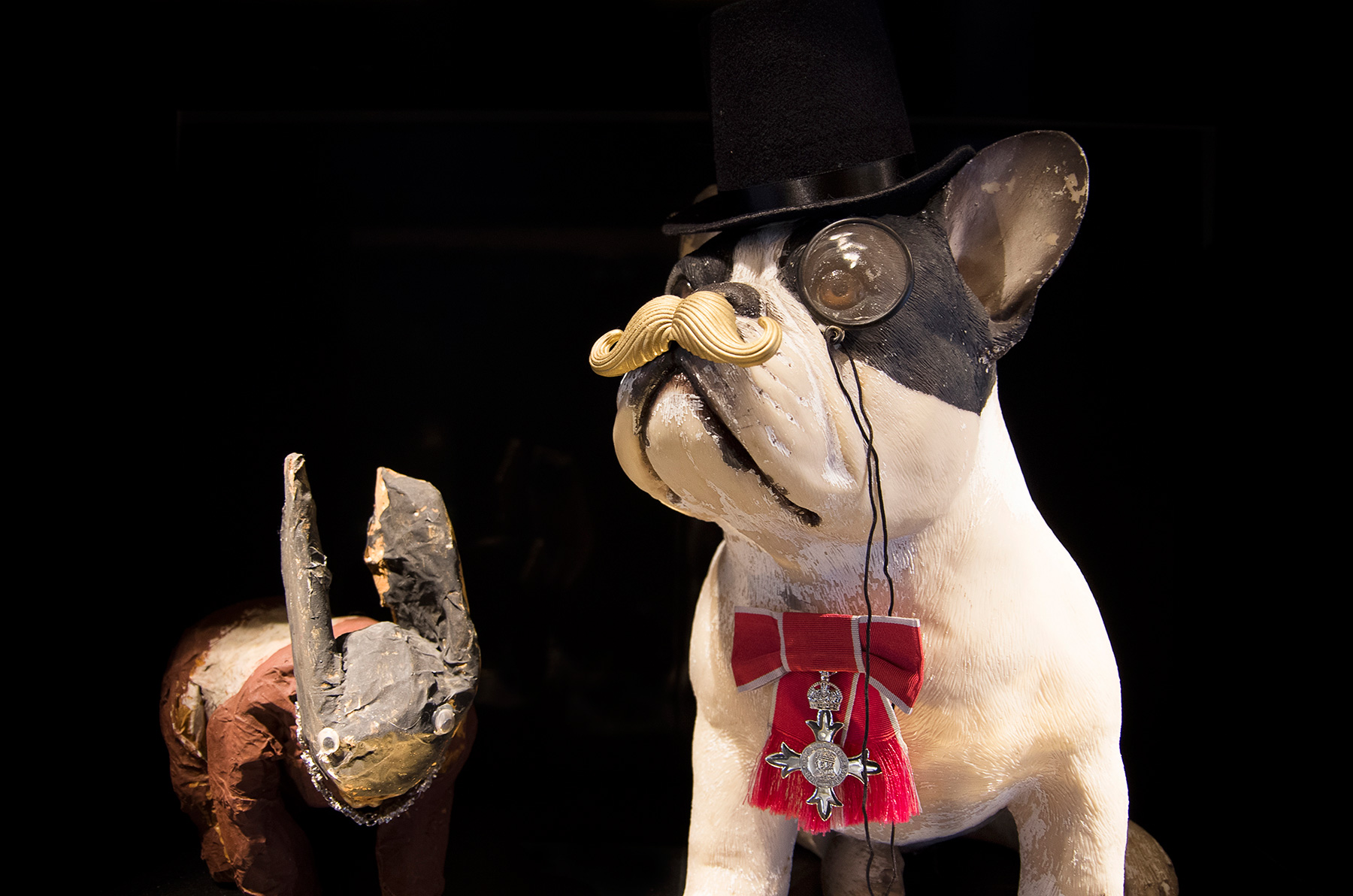 Annoushka Milestones Exhibition display cabinet - Annoushka's son's papier mache dog and a plastic french bulldog wearing a top hat, monacle, moustache and Annoushka's MBE
