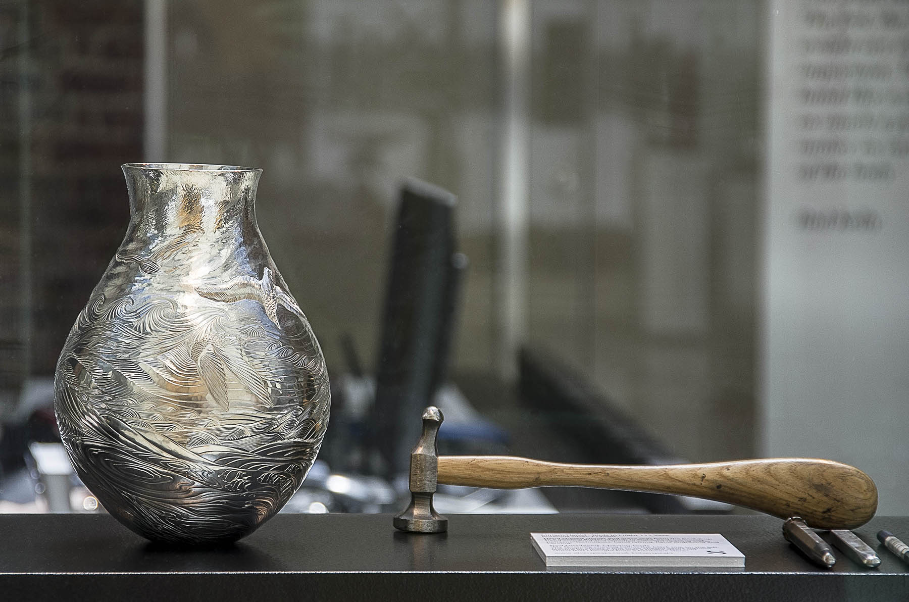 Silver Speaks Form Exhibition display case - Miriam Handid chased sterling silver vase (swirls of sea, clouds and birds) with chasing hammer
