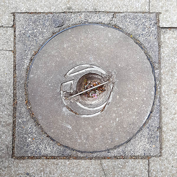 Manhole Cover, London - Cast iron rim and concrete centre with asymmetrical swirl surrounding dirt hole