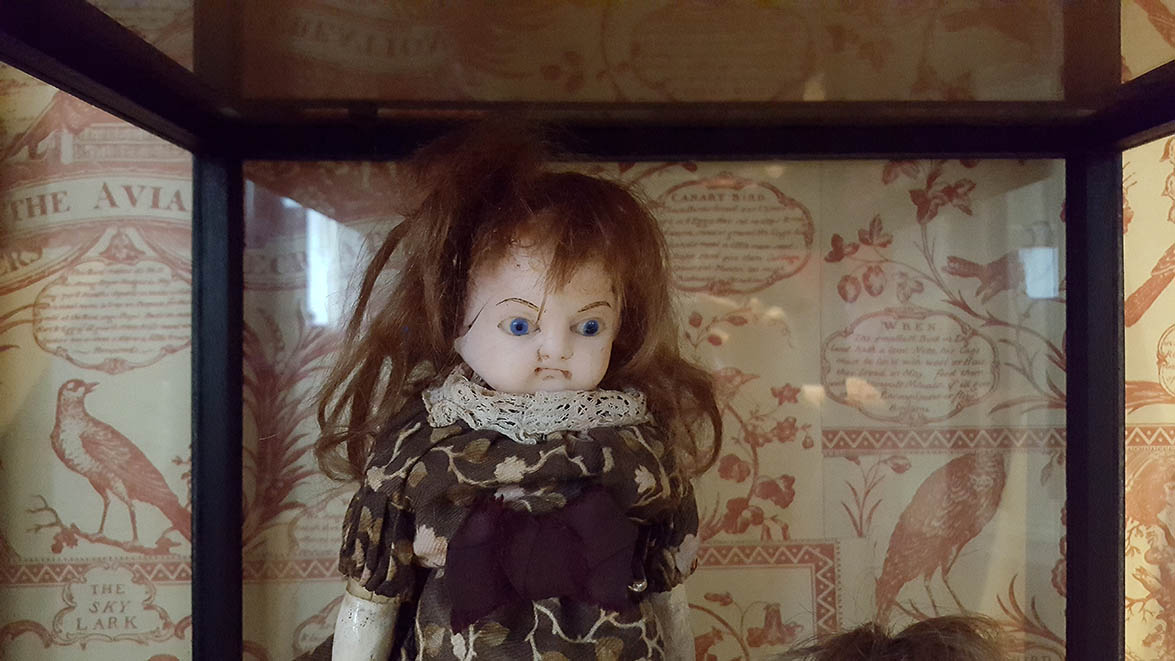 Angry looking ceramic doll in glass display case in Pollocks Toy Museum