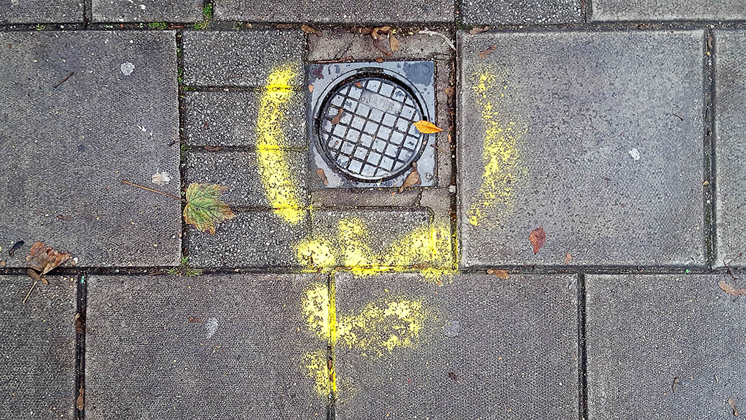 Pavement markings - spray painted squiggles on paving stones - yellow lines surround metal access plate