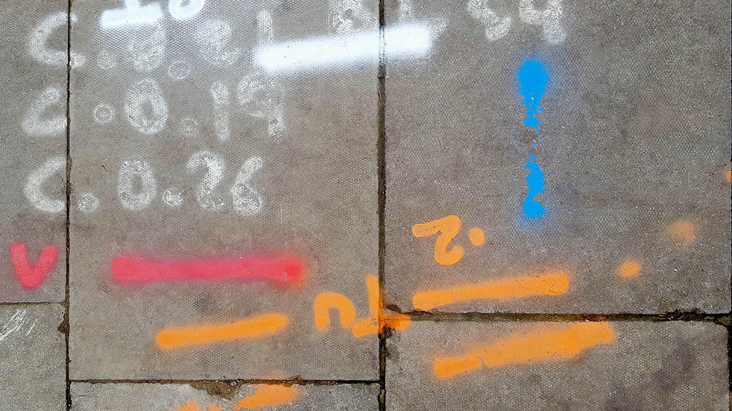 Pavement markings - spray painted squiggles on paving stones - Orange white red blue lines and numbers