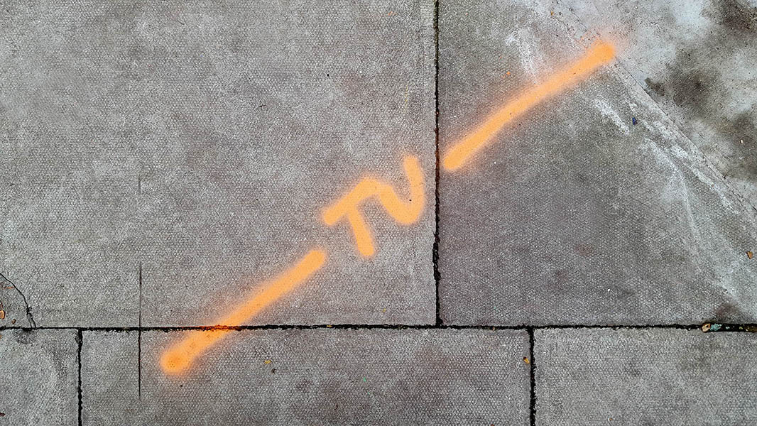 Pavement markings - spray painted squiggles on paving stones - Orange diagonal line and letters TV