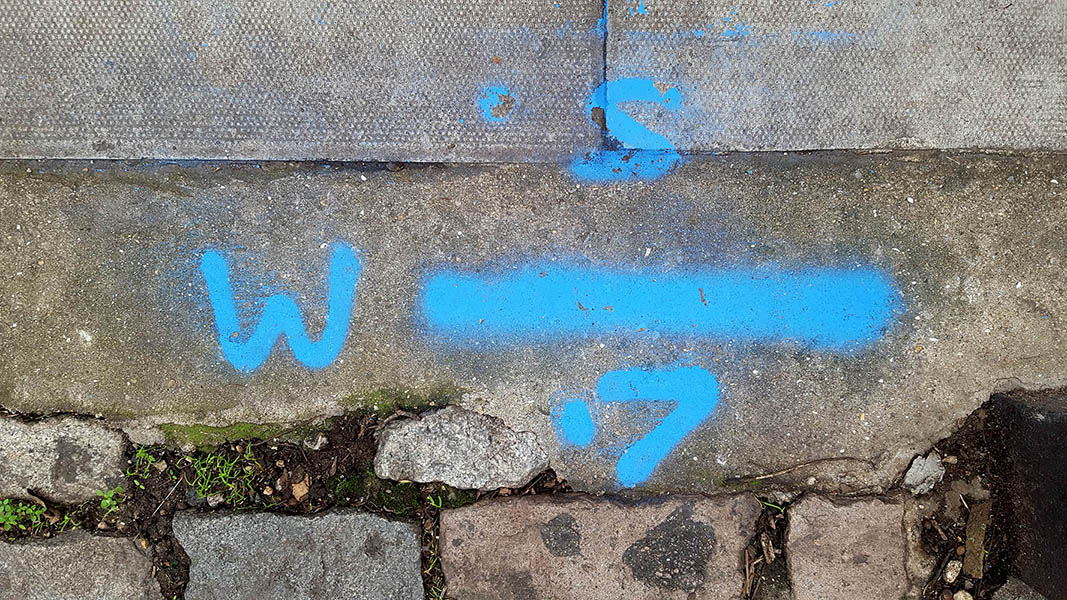 Pavement markings - spray painted squiggles on paving stones - Blue line numbers and letters
