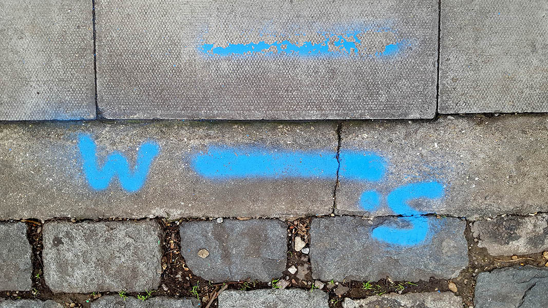 Pavement markings - spray painted squiggles on paving stones - Blue lines letters and numbers