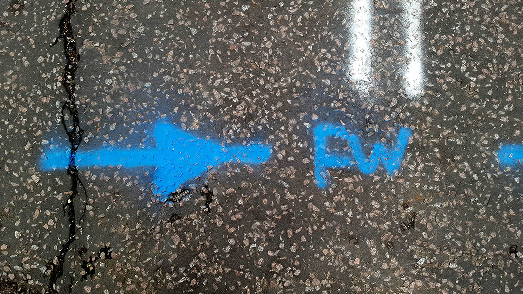 Pavement markings - spray painted squiggles on tarmac - Blue arrow and letters and white lines