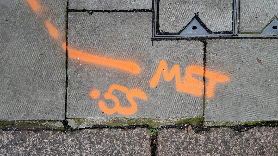 Pavement markings - spray painted squiggles on paving stones - Orange lines letters and numbers