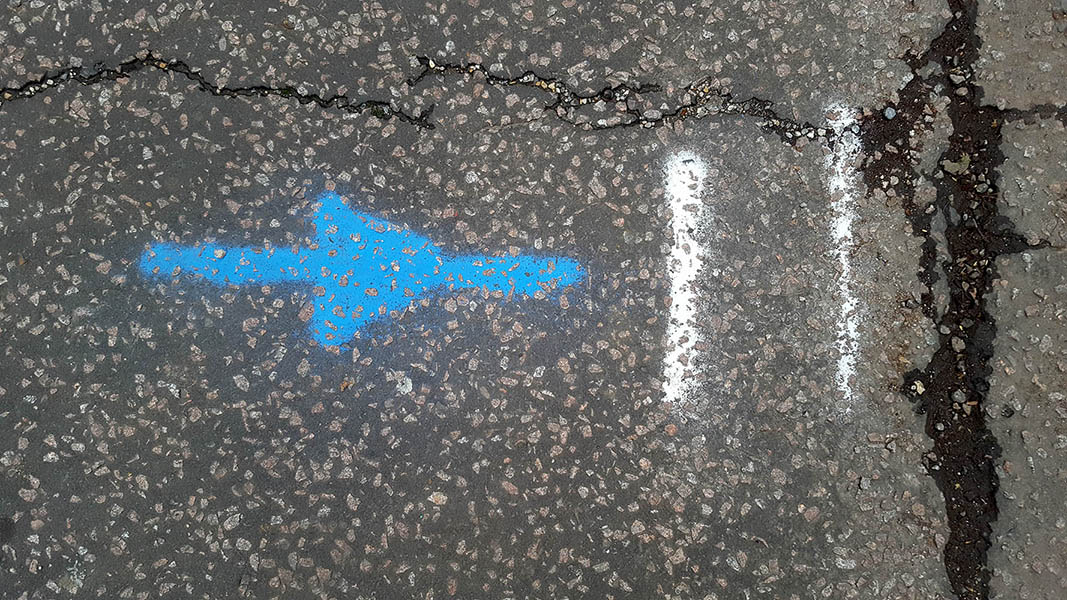 Pavement markings - spray painted squiggles on tarmac - Blue horizontal arrow and white vertical lines