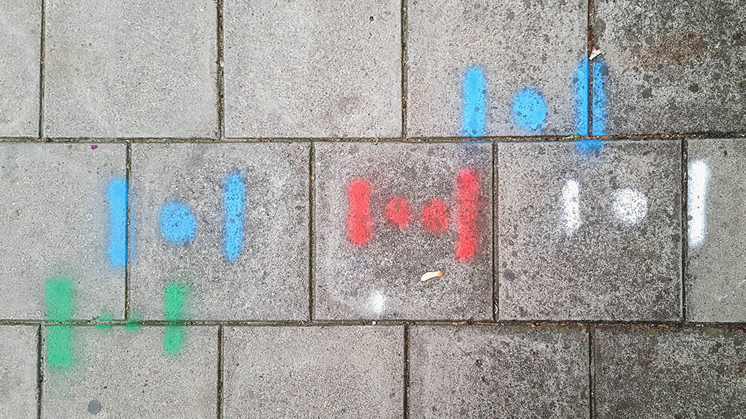 Pavement markings - spray painted squiggles on paving stones - Dot flanked by horizontal lines in five groupings of green, red, white and two blue 