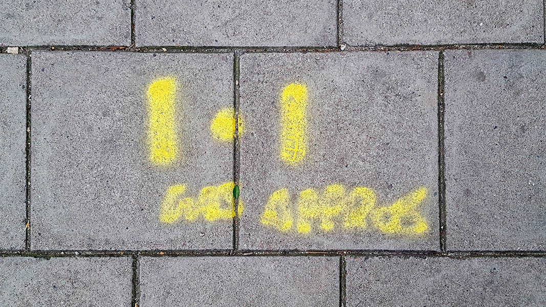 Pavement markings - spray painted squiggles on paving stones - Yellow dot flanked by vertical lines above illegible writing