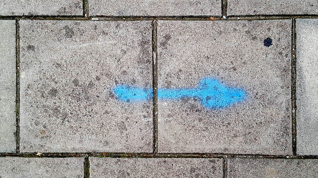 Pavement markings - spray painted squiggles on paving stones - Blue arrow pointing right