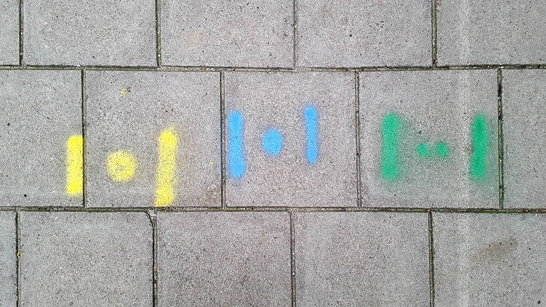 Pavement markings - spray painted squiggles on paving stones - Dot flanked by vertical lines in three groupings of yellow, blue and green