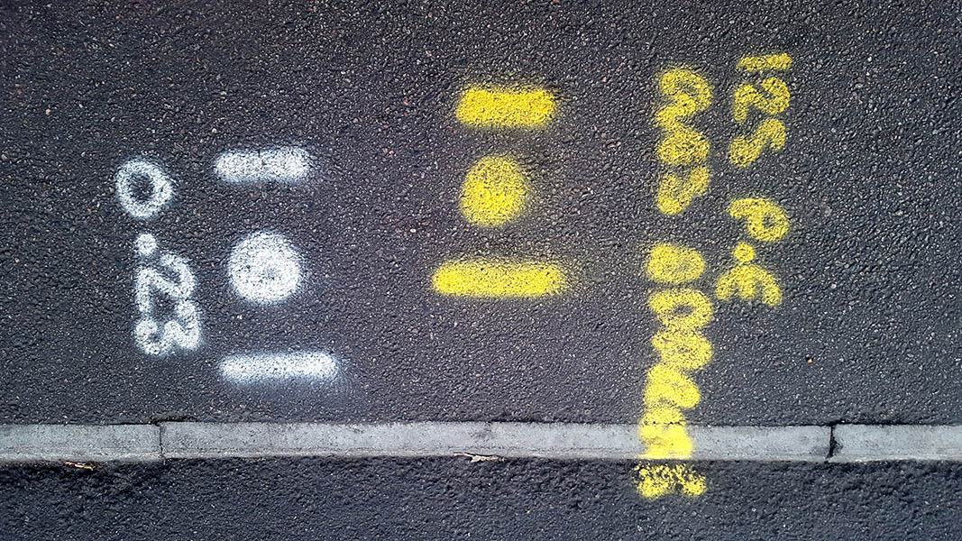 Pavement markings - spray painted squiggles on tarmac - Yellow and white letters dots and lines