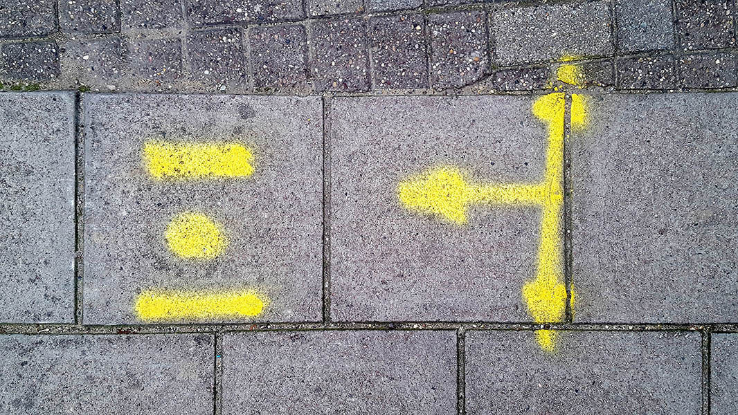 Pavement markings - spray painted squiggles on paving stones - Yellow dot flanked by horizontal lines beside three headed arrow pointing up, down and left