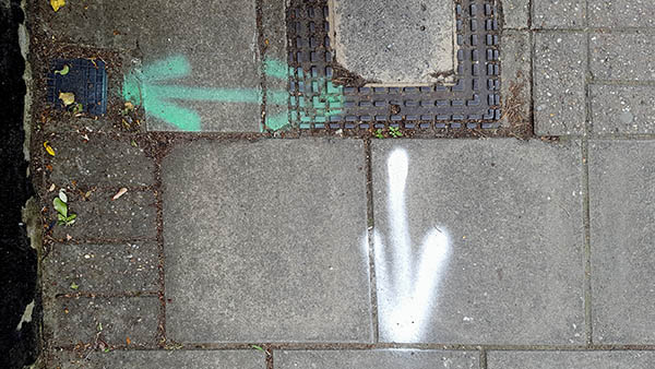 Pavement markings - spray painted squiggles on paving stones - Green horizontal arrow and white vertical arrow