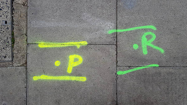 Pavement markings - spray painted squiggles on paving stones - Yellow dot and letter P flanked by two lines with green dot and letter R flanked by two lines