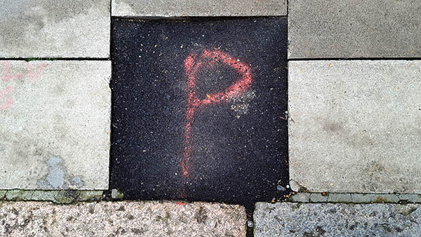 Pavement markings - spray painted squiggles on paving stones - Red letter P in a black tarmac square 