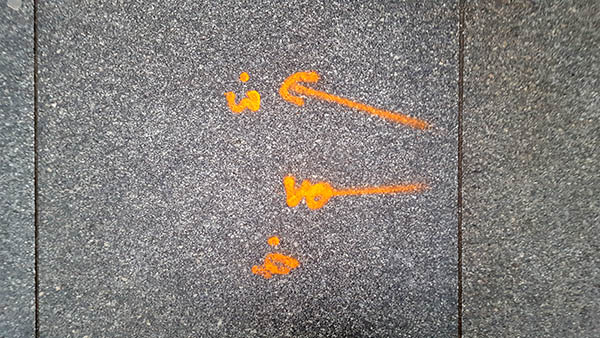 Pavement markings - spray painted squiggles on paving stones - Orange arrows and numbers