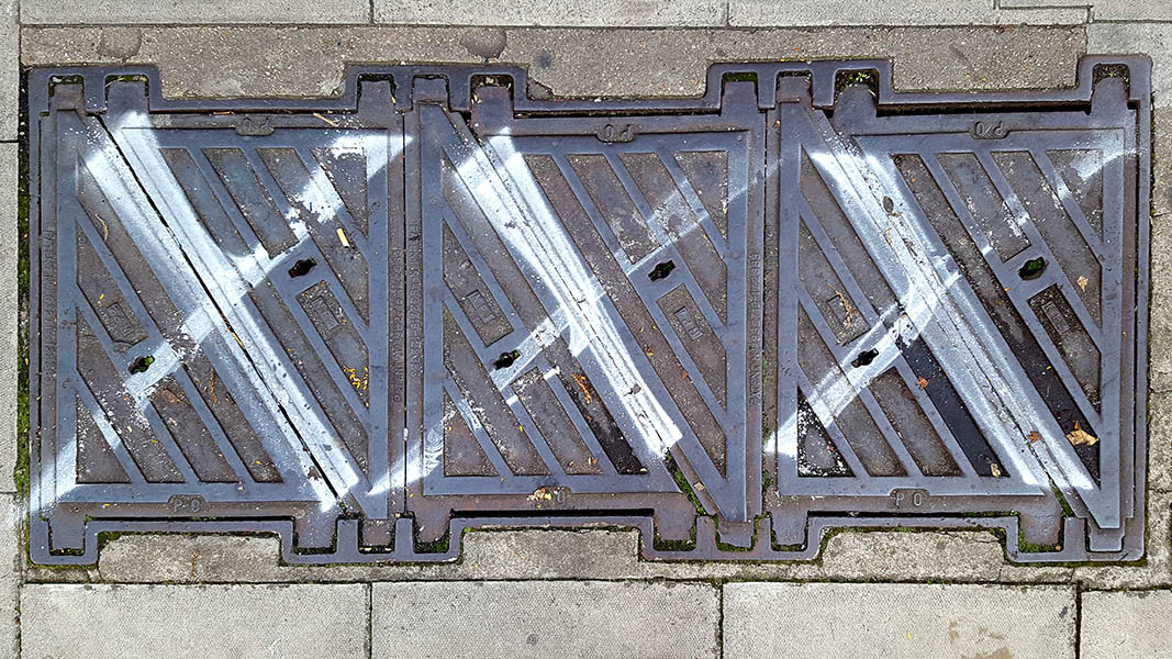 Pavement markings - spray painted squiggles on paving stones - Three large square metal PO access panels with a white diagonal cross through each