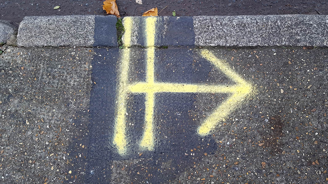 Pavement markings - spray painted squiggles on concrete pavement - Large yellow arrow pointing to the left with two vertical lines at the base