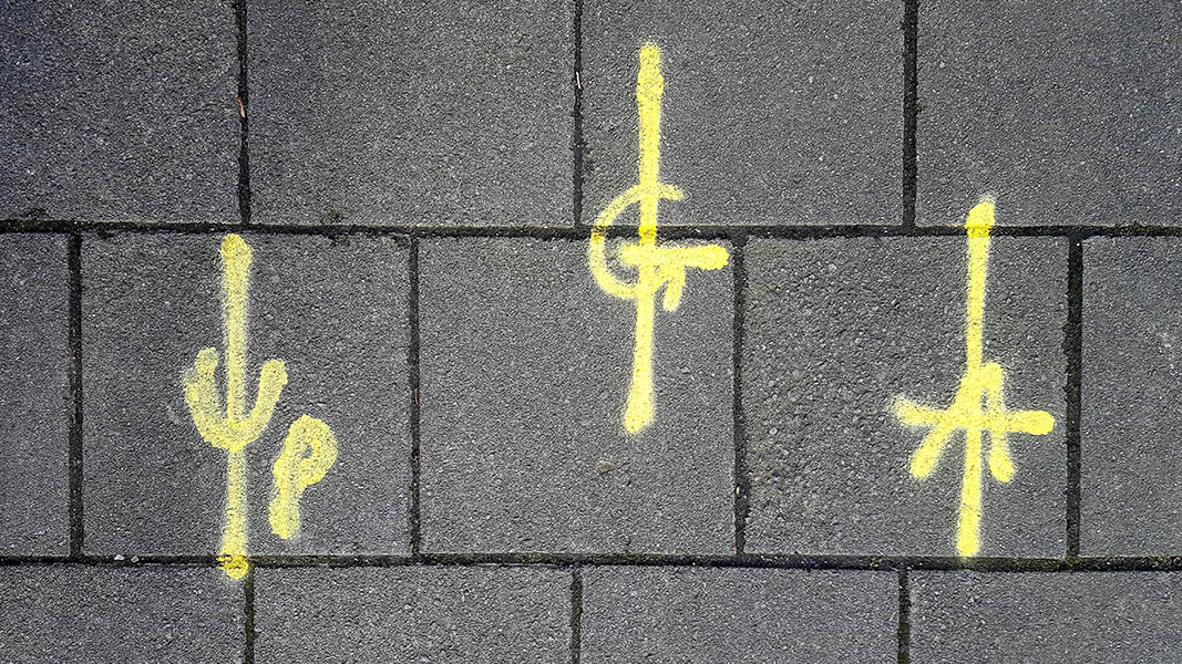 Pavement markings - spray painted squiggles on paving stones - Three yellow staggered vertical lines with letters in the centre - UP, left, G centre and A right