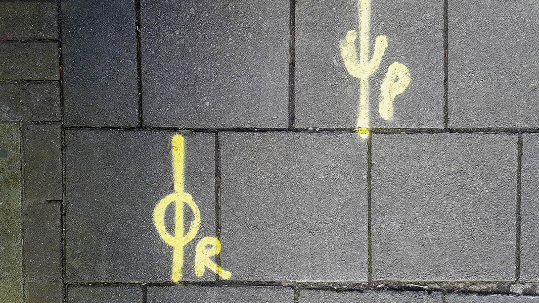 Pavement markings - spray painted squiggles on paving stones - Two yellow staggered vertical lines with letters in the centre - OR, left and UP, right