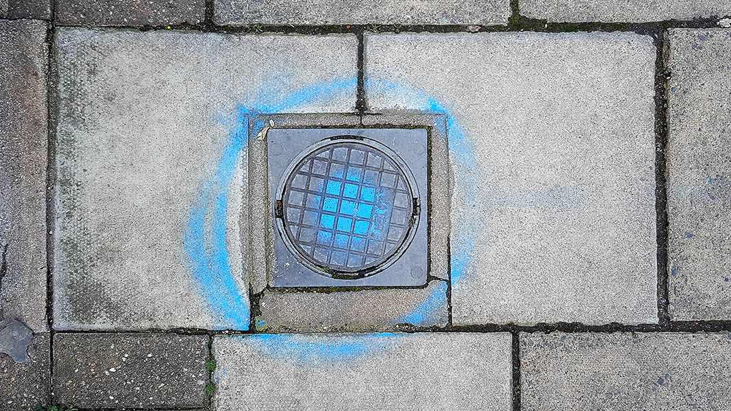 Pavement markings - spray painted squiggles on paving stones - Small water access plate with a central blue dot and surrounded by circle