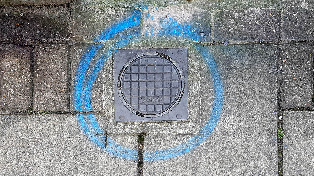 Pavement marking - spray painted squiggles on paving stones - Small water access plate surrounded by blue circle