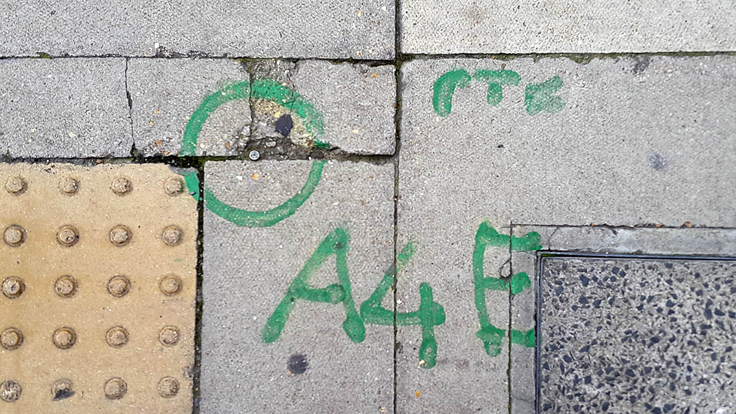 Pavement markings - spray painted squiggles on paving stones - Metal rivet surrounded by green circle above A 4 E