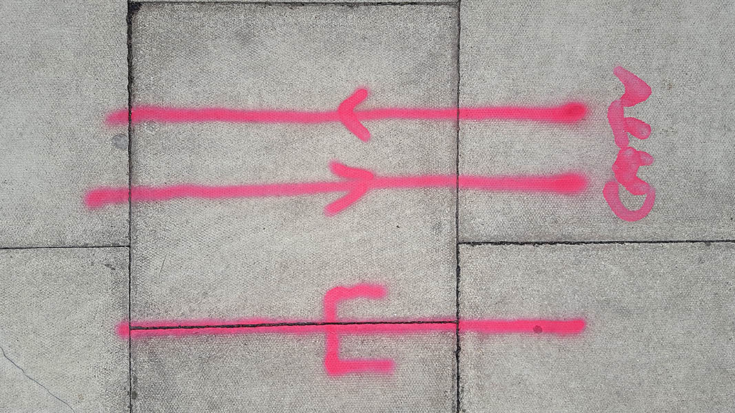 Pavement markings - spray painted squiggles on paving stones - Red lines arrows and writing