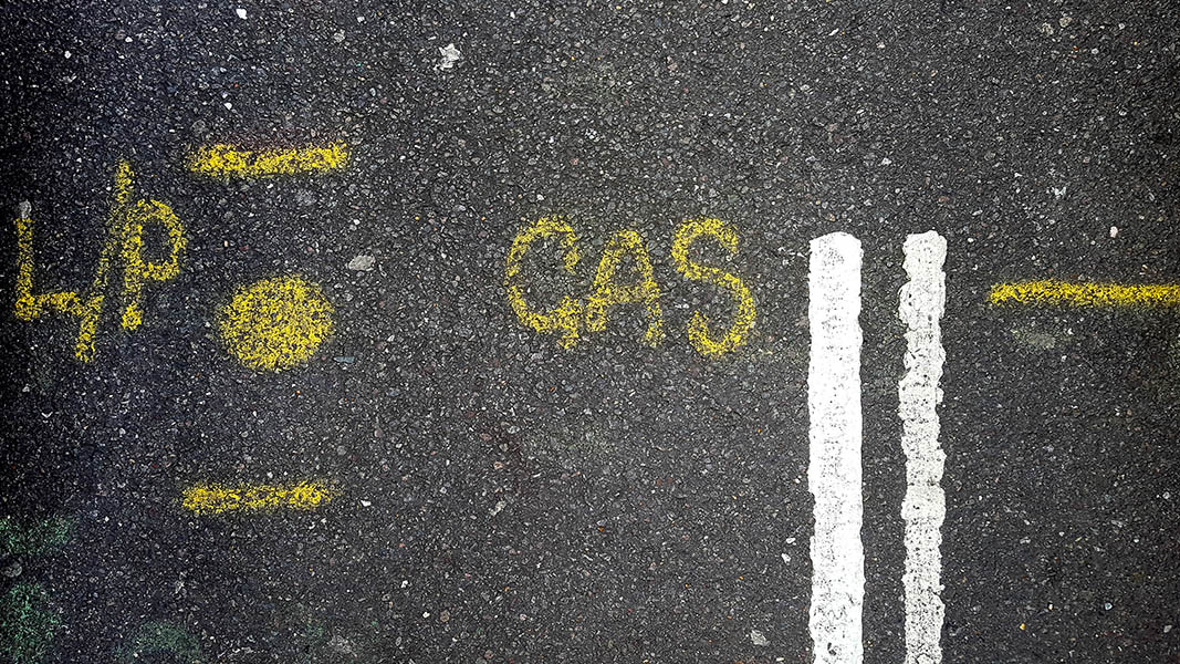 Pavement markings - spray painted squiggles on tarmac road - Yellow dot sandwiched between horizontal lines L/P to the left and GAS to the right